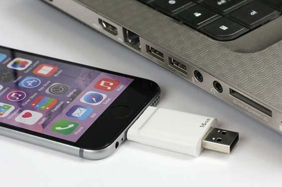 iphone with a USB Drive plugged into it sitting next to a laptop.