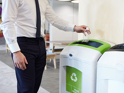 Man in office throwing bottle in recycling bin.